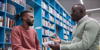 an African American student sits with an advisory in a library to discuss classes and academic progress