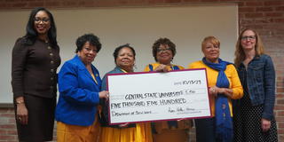 six people smile at the camera while four of them hold a large check during a ceremony honoring the late Mit Joyner, former NASW president, at Central State University