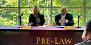 two people sit at a table with a tablecloth reading "Pre-Law" in front of windows with trees outside