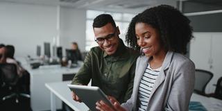 Smiling young african american professional businessman and businesswoman together working online with a digital tablet in office