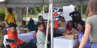 a large group of people sits under a tent at the 2023 land-grant open house at central state university