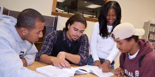 four central state university students with open books at a table during a study session