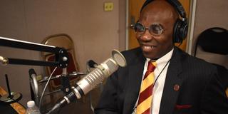morakinyo a.o. kuti with a maroon and gold striped tie using broadcast equipment for a podcast