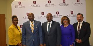a group of people including united states department of agriculture chief terry crosby stand in front of a large central state university backdrop