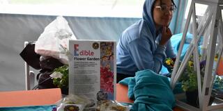 a young person in a blue hoodie sits behind a table displaying an edible flower garden