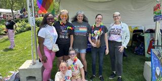 seven people of all ages under a tent with a progress pride flag flying at cleveland pride