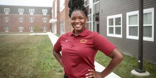 A young Black woman in maroon stands with hands on hips in front of residence halls at Central State University