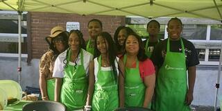 eight youth and adults wearing green aprons at a farmers market