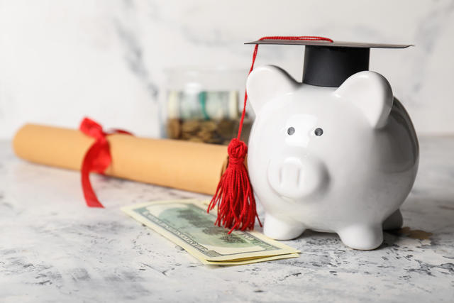 Piggy Bank wearing a graduation cap next to a diploma and money