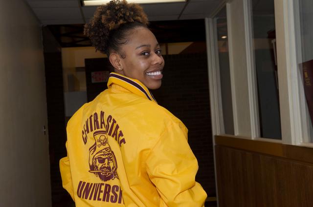 a central state university marauder looks back over their right shoulder, smiling at the camera. they are wearing a central state jacket in maroon and gold