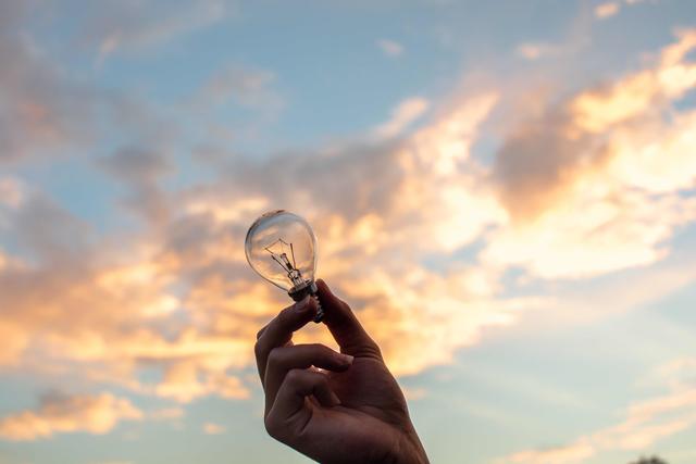 closeup of a hand holding a lightbulb with a bright sky in the background