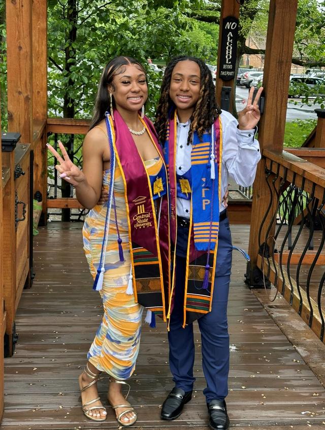 Two young Black women in honors sashes give a peace sign to the camera
