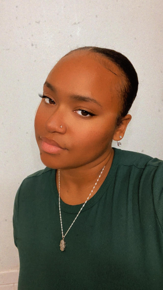 A young woman wearing a gold necklace and forest green shirt