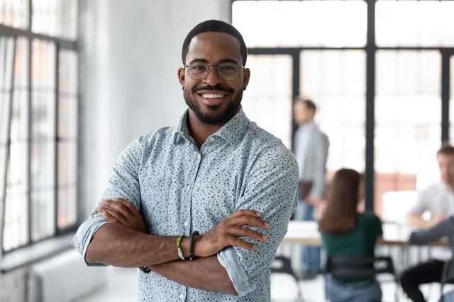 Black small business owner in a button-down shirt with arms crossed in an office setting