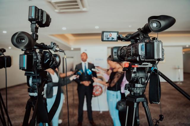 several people conduct on-camera interviews while standing around the subject being interviewed with two cameras in the foreground