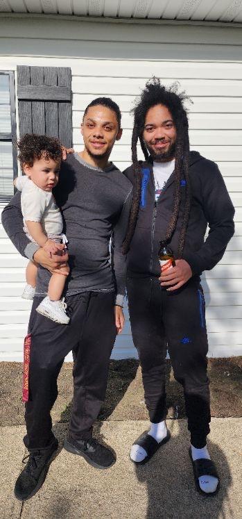 two young Black men with one holding a baby