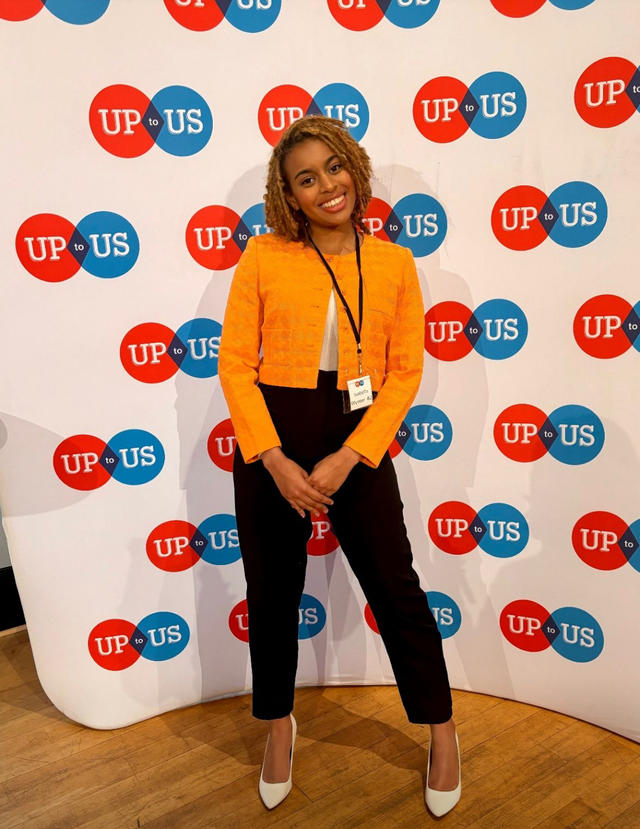 isabella wynter wears an orange top and black pants while standing in front of a backdrop