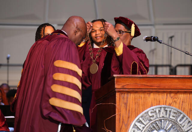doctor kuti bends forward while central state university board of trustees chair jacqueline gamblin places the medallion over his shoulders
