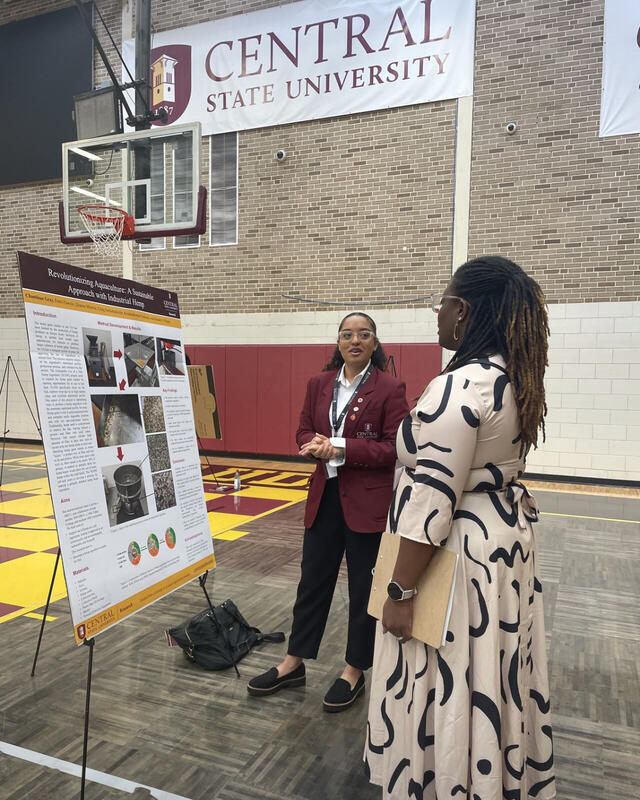 chantinae gray with a research poster standing with dr. sarah armstrong-jones under a central state university banner
