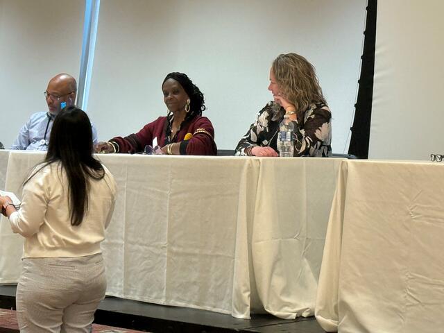 three panelists sit at tables with white tableclothes