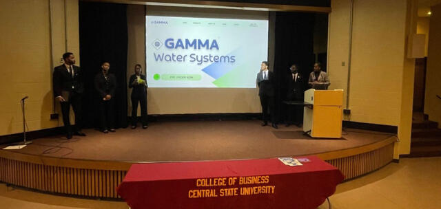 students presenting on stage with gamma water systems on the big screen