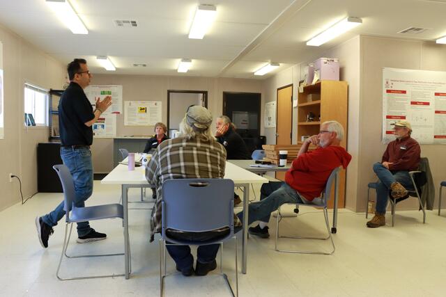 workshop participants sit around a table while a researcher speaks to them