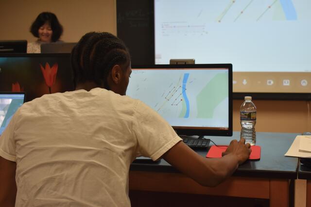 the back of a young african american man working with drone software on a laptop in a computer lab