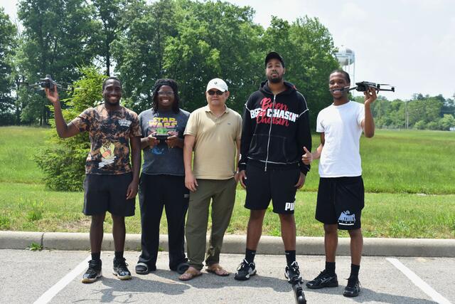 five people stand in a line near an open green space