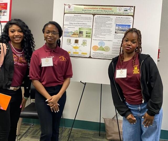 students stand beside a research poster