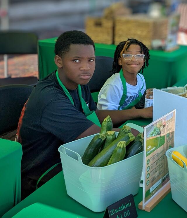 two young people with produce at a farmers market