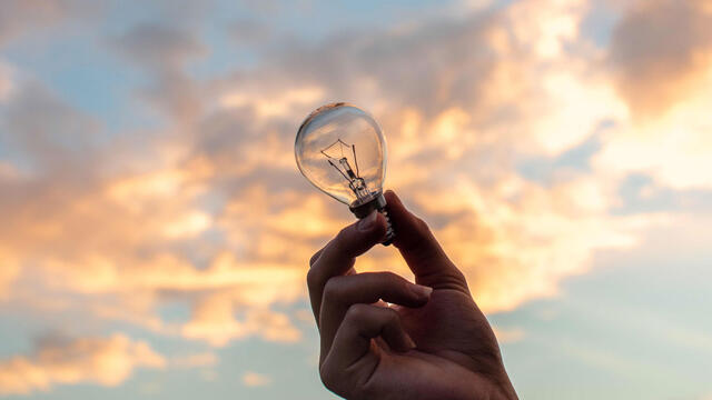 closeup of a hand holding a lightbulb with a bright sky in the background